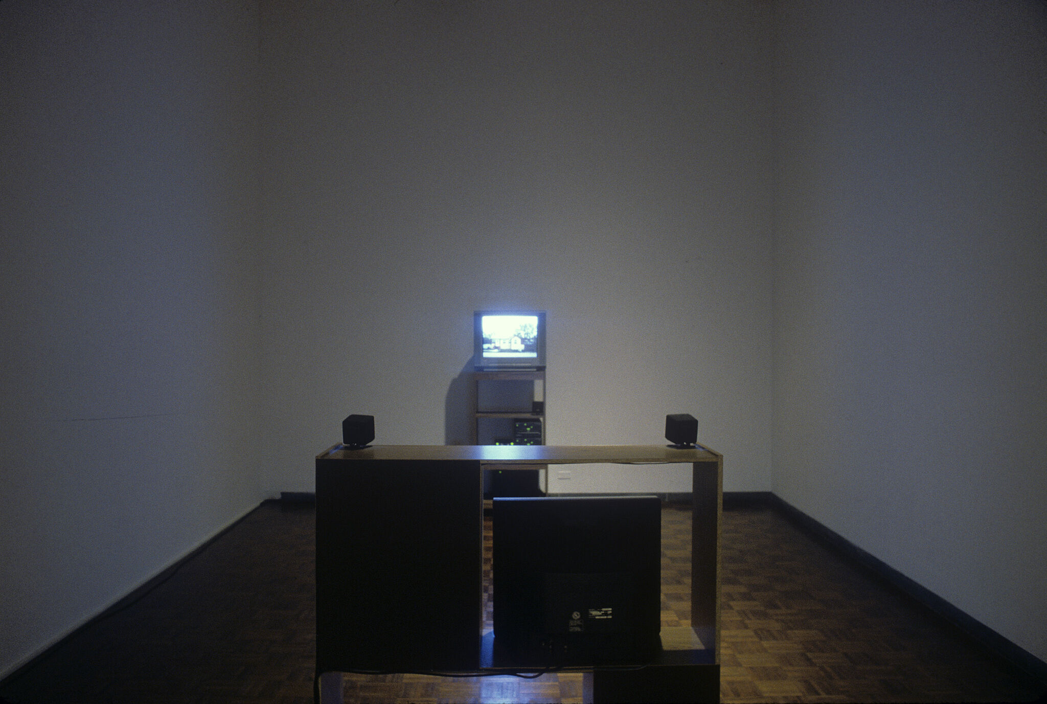 A gallery with an installation made up of a small television set with a shelf displayed in front of it.