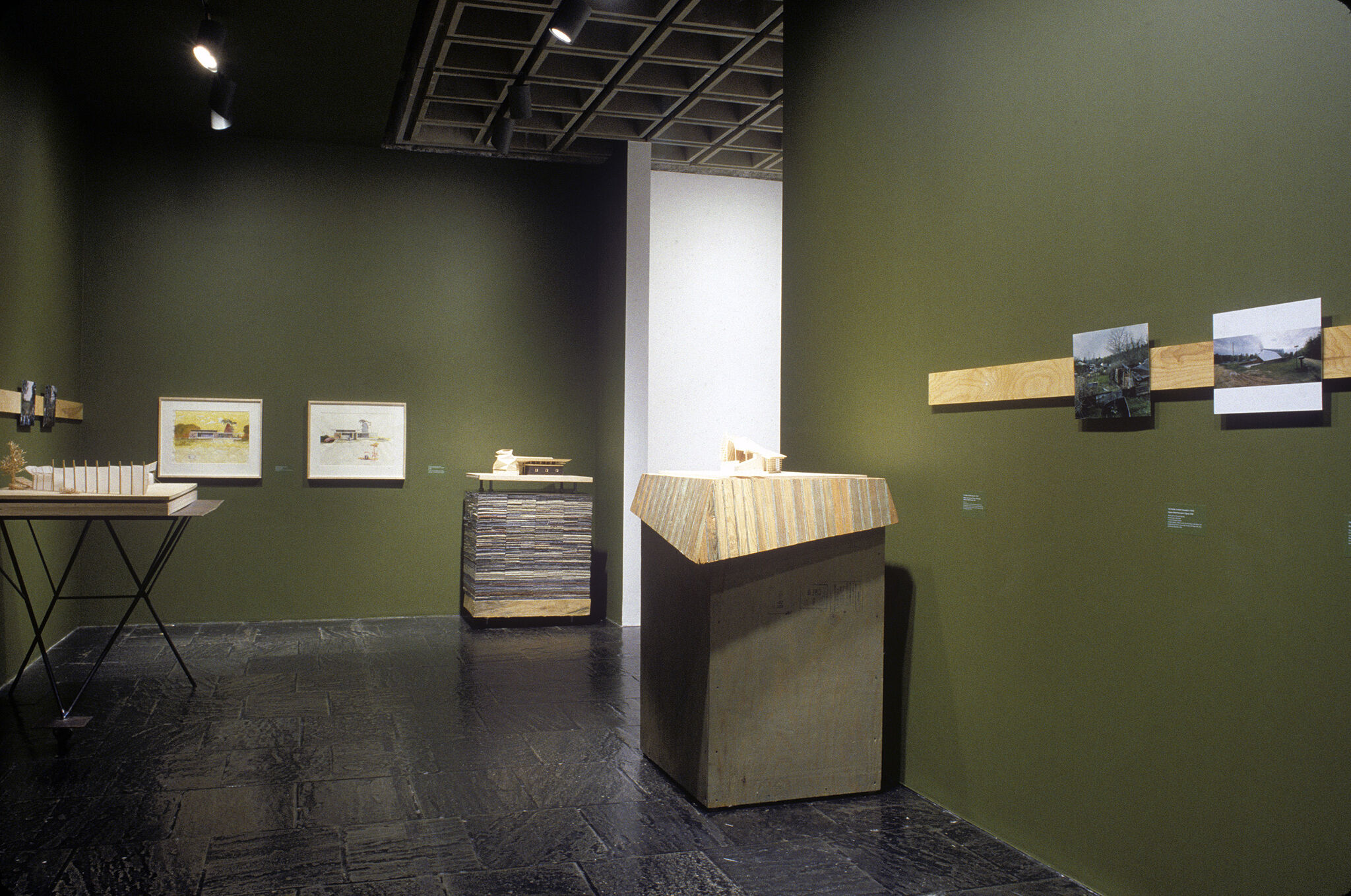 A gallery with green walls filled with various works of art, including photographs and sculptures.