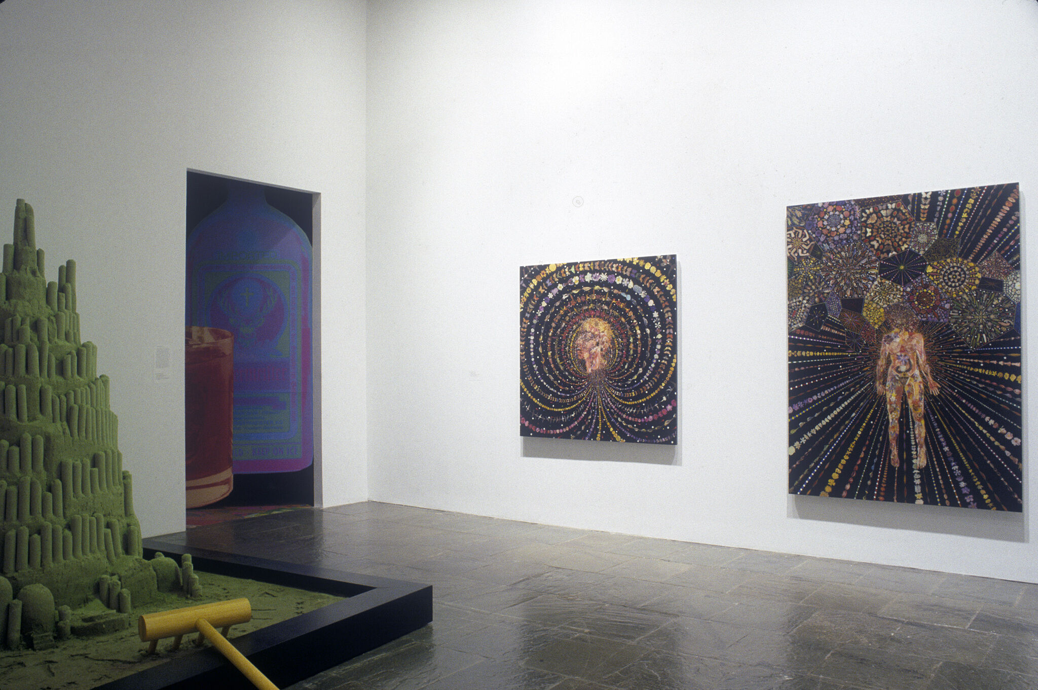 Three abstract paintings displayed in a gallery along with a green sculpture.