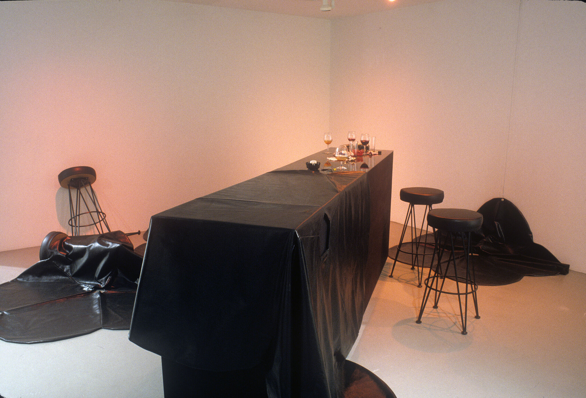 A long table covered in a black tablecloth, displayed with wine glasses along with black stools.