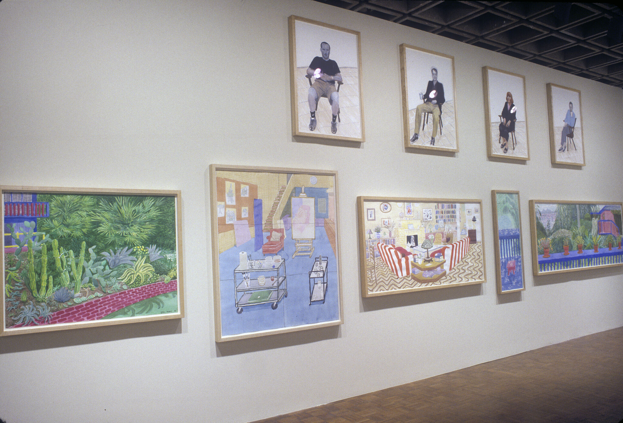 A wall in a gallery filled with art work by David Hockney.