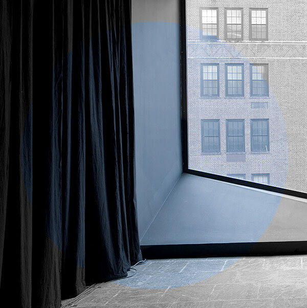 A large window with a view of a brick building, partially covered by dark curtains.