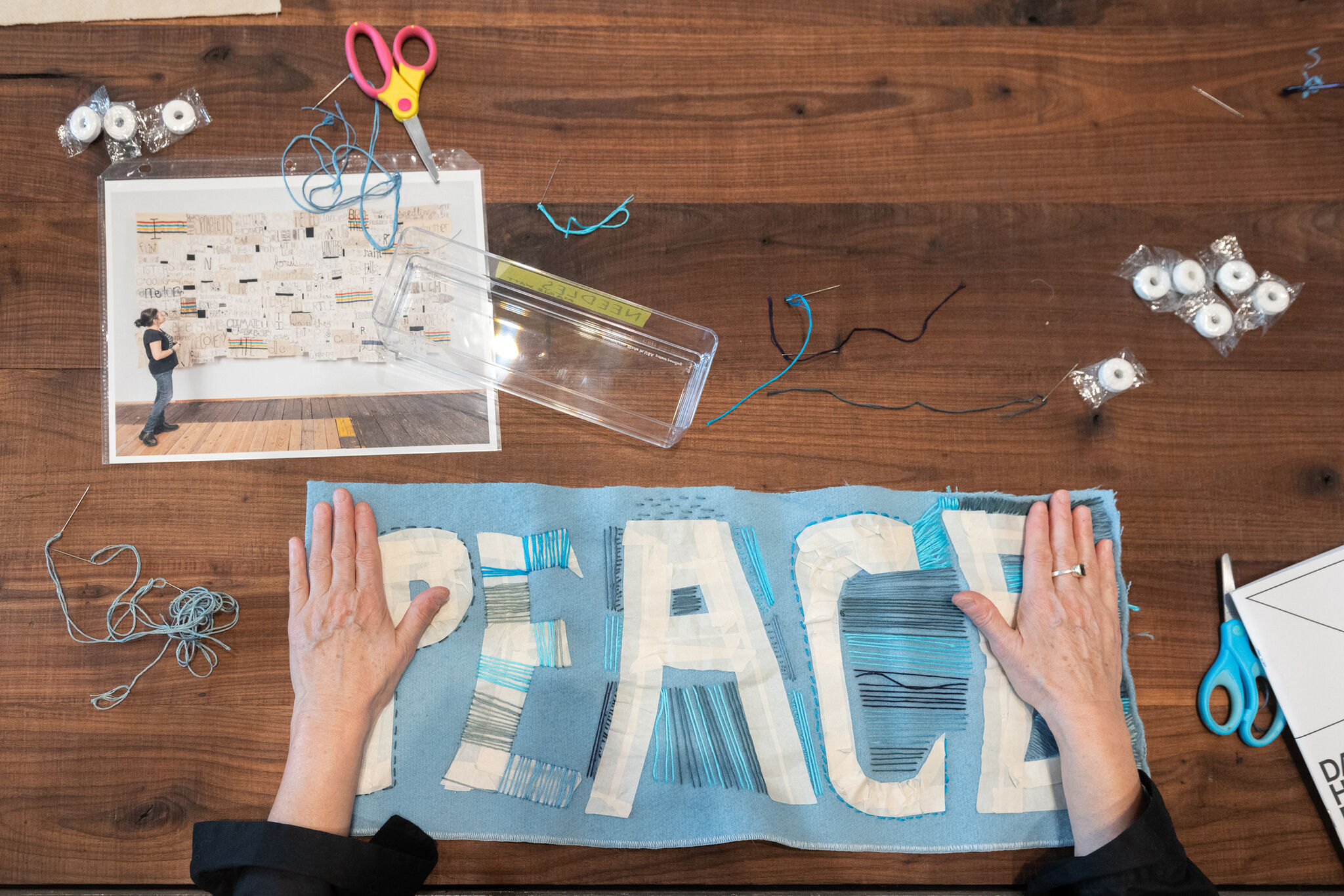 Hands work on a textile artwork that says peace. 