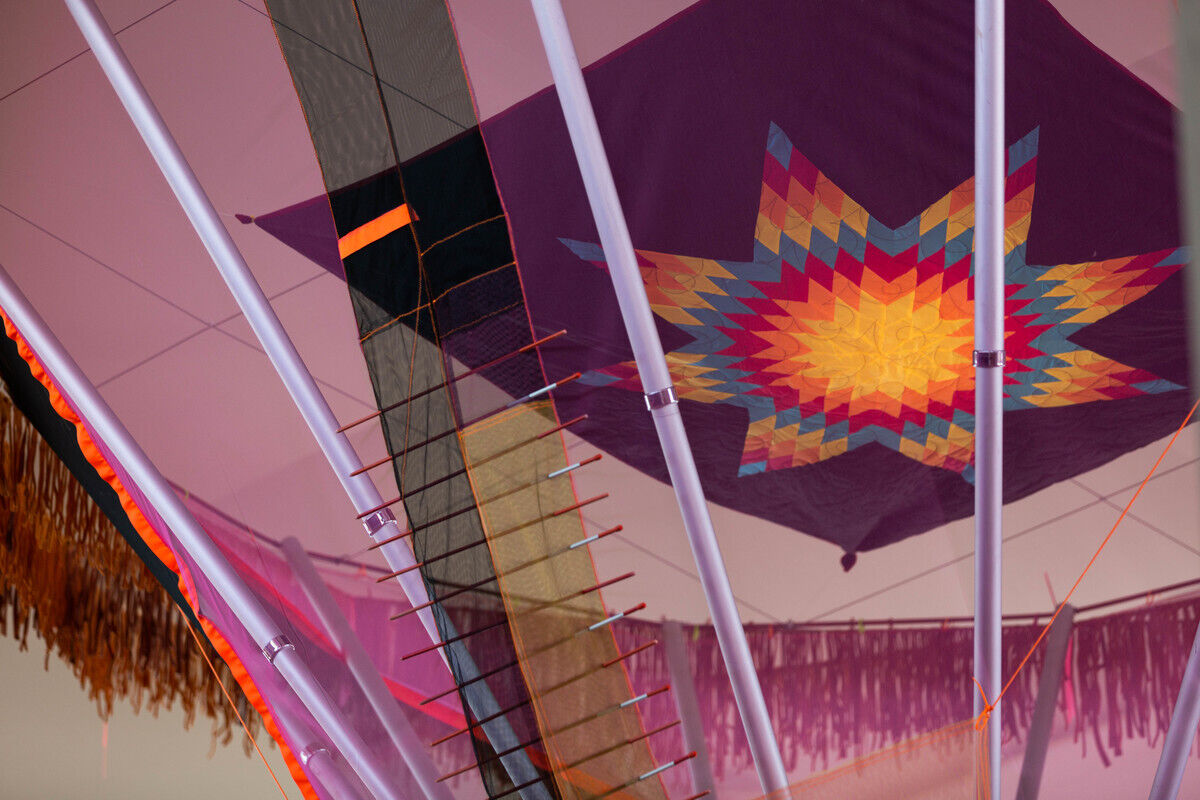 Colorful quilted artwork displayed between white poles with a warm, glowing ambiance.