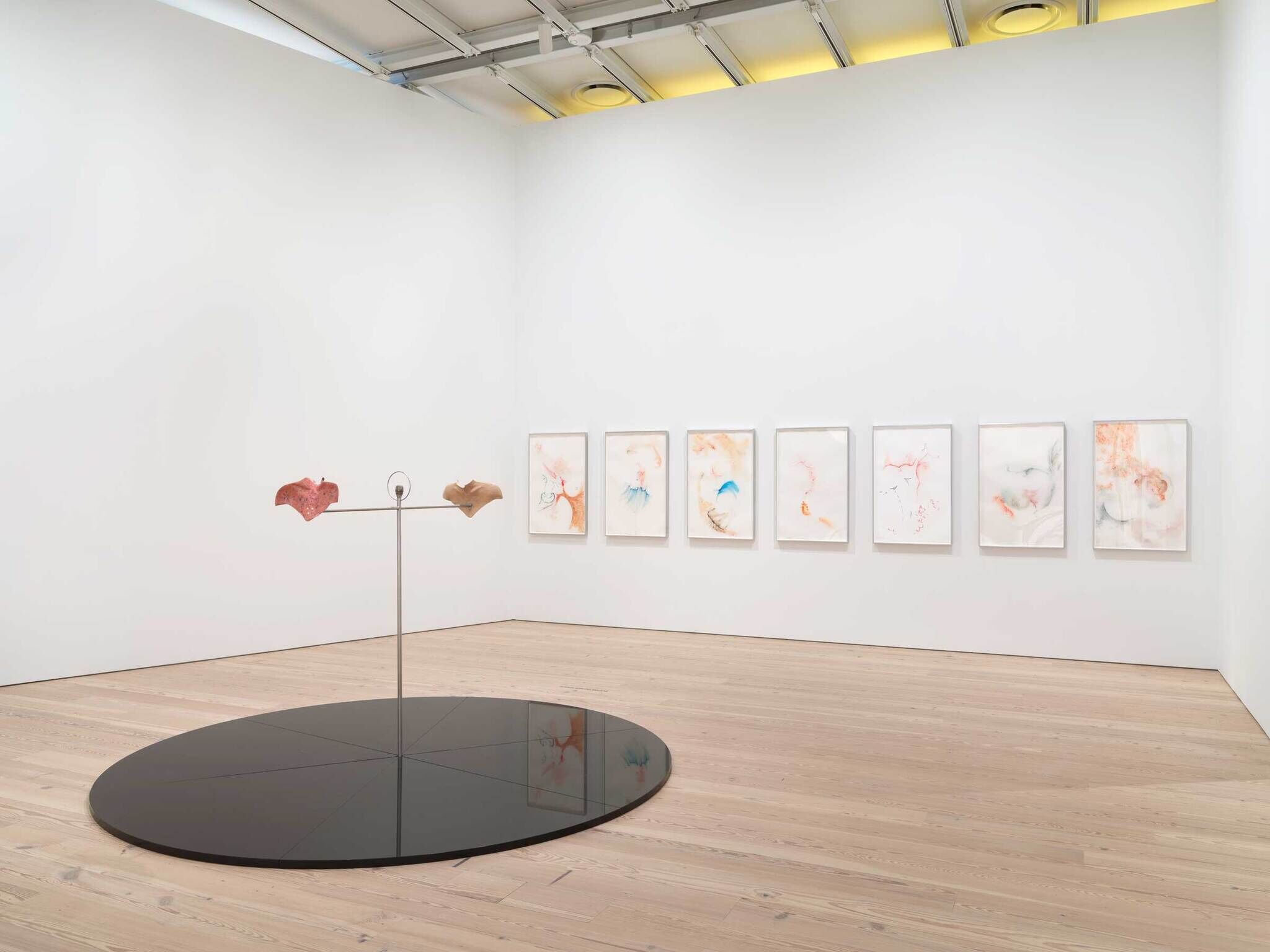 Modern art gallery interior with abstract paintings on wall and a kinetic sculpture with two colorful shapes on a reflective black disc.