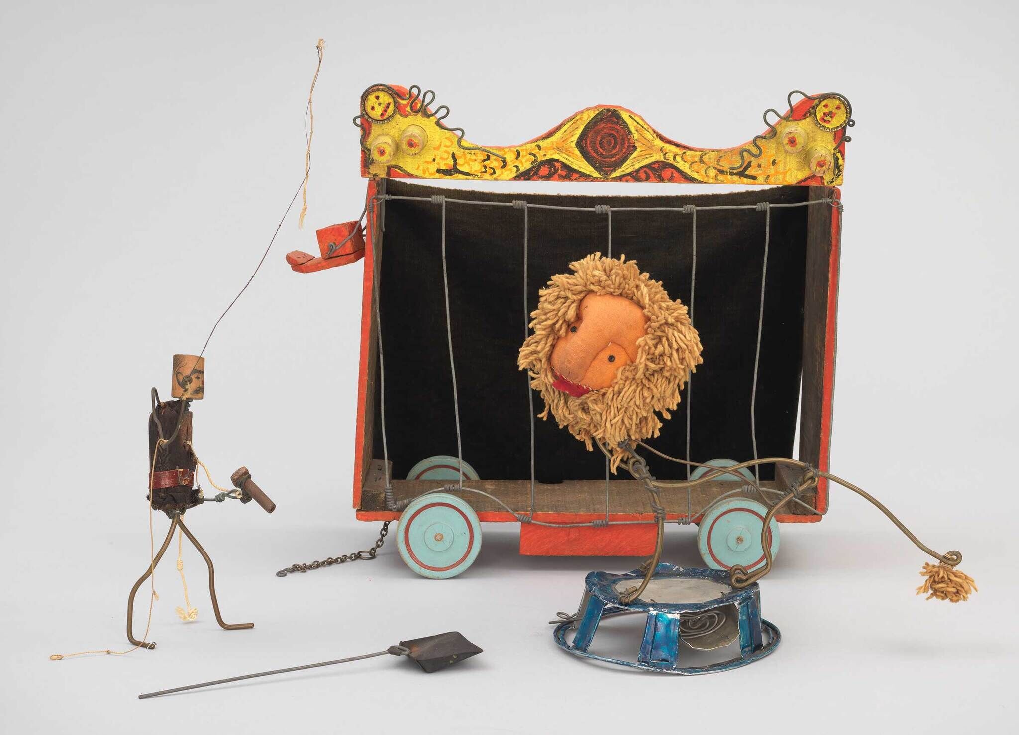 A handmade circus scene with a wire lion tamer and a lion puppet in front of a colorful cage.