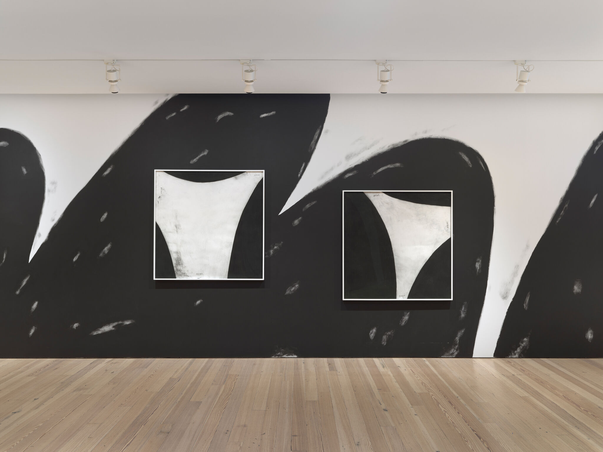 Two abstract black and white paintings on a wall with sweeping brushstrokes, displayed in a gallery with wooden flooring.
