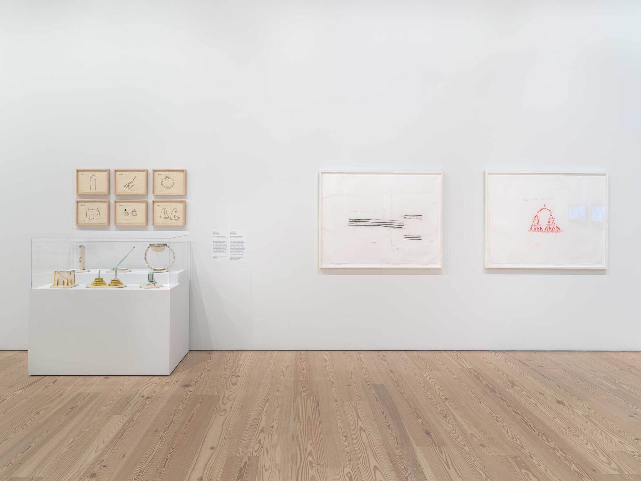 Art gallery wall with framed sketches and a display case of small sculptures on a wooden floor.