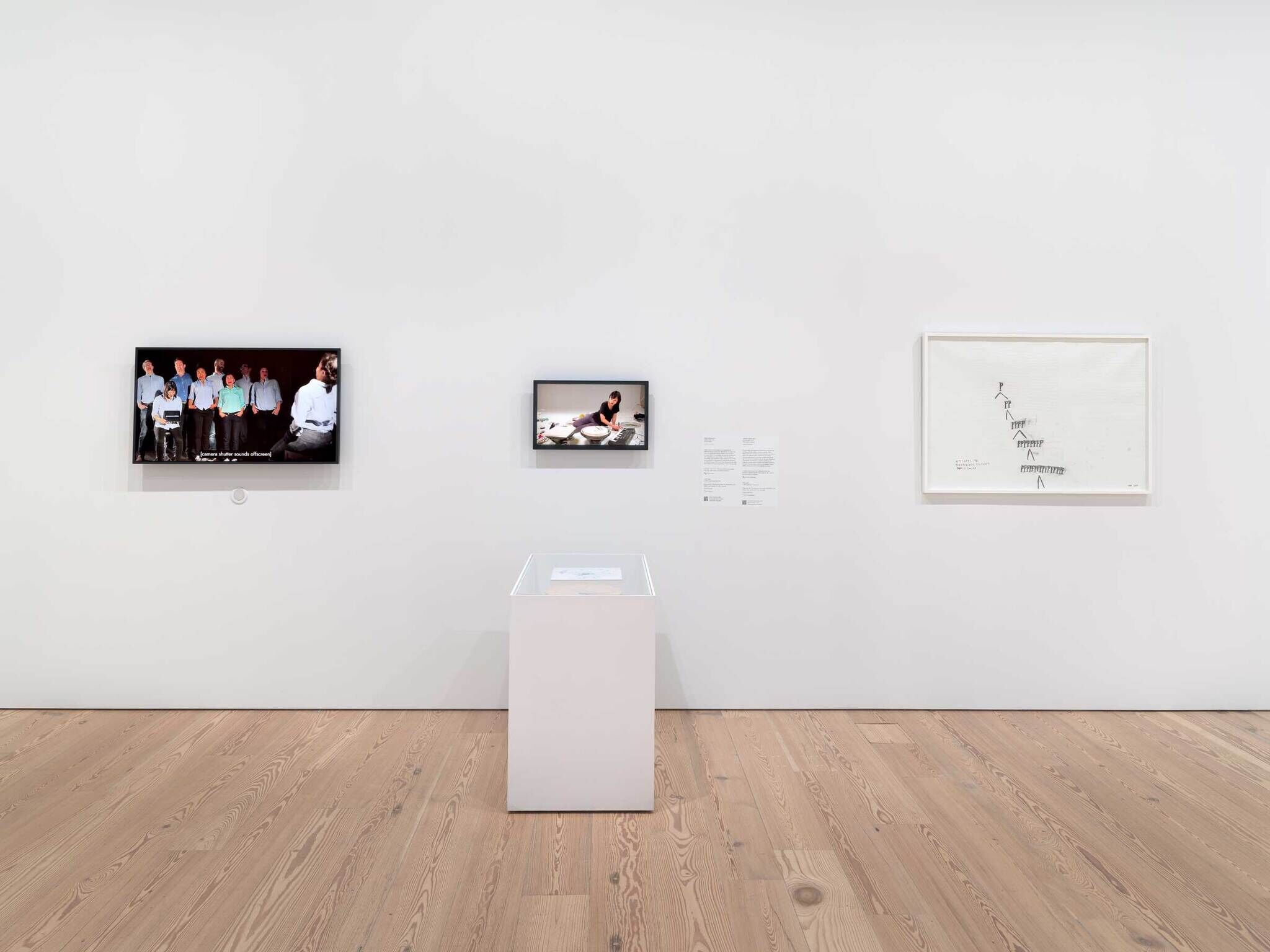 Art gallery wall with three framed pieces and a display case on a wooden floor.