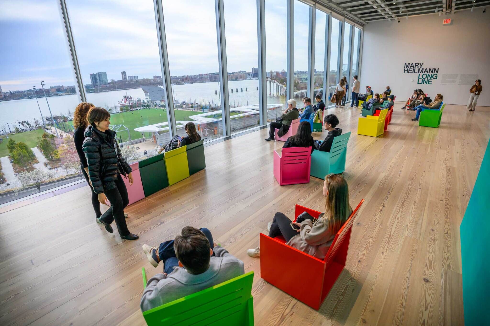 People sitting in multicolored chairs looking out at a soccer field and the Hudson river.