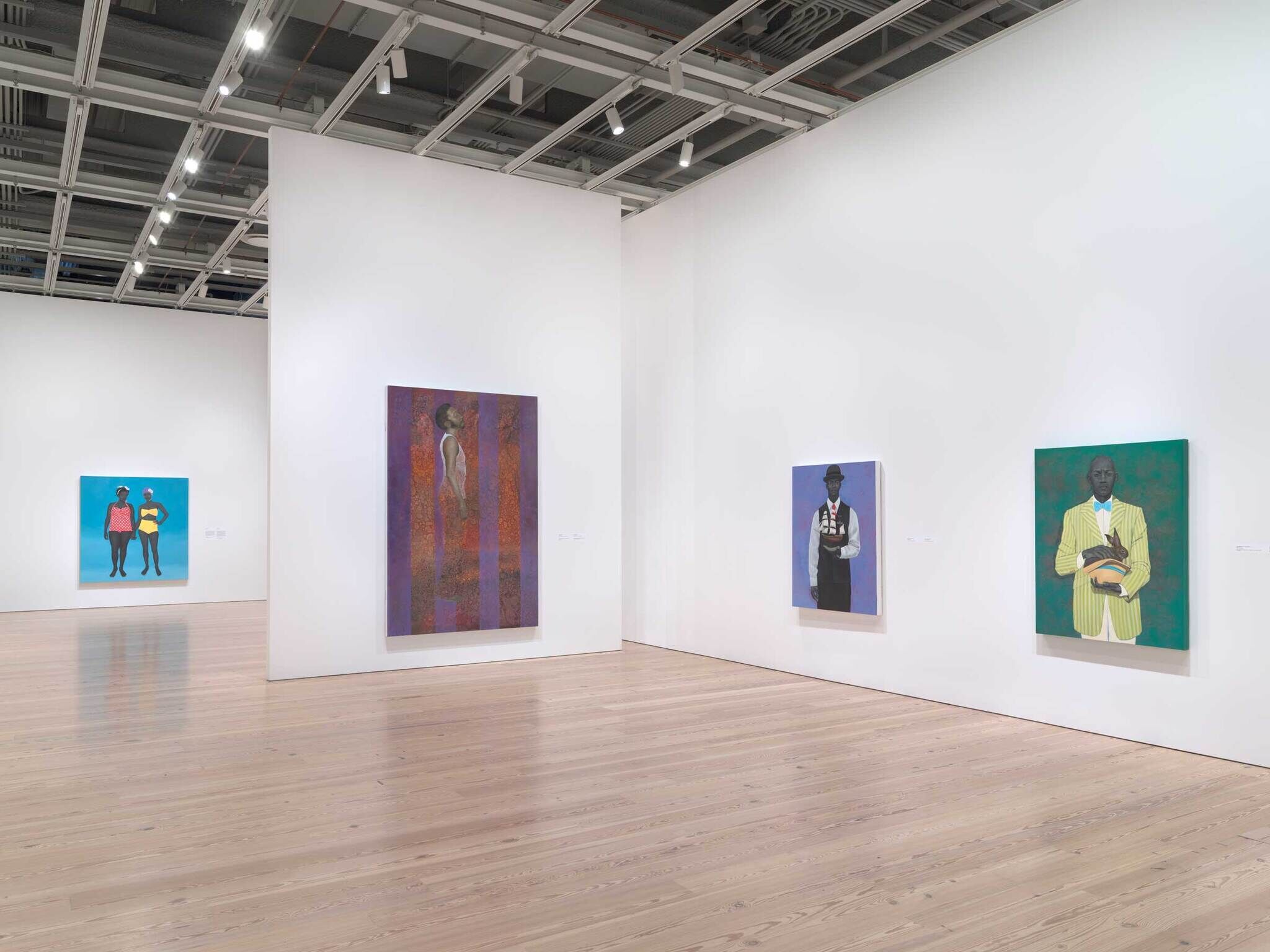 Art gallery with four colorful paintings of people displayed on white walls in a spacious, well-lit room.