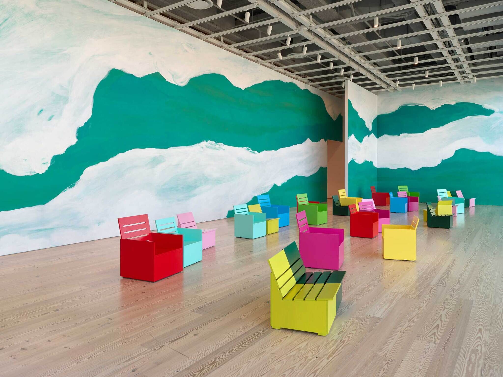 Brightly colored chairs are arranged in a spacious room with green and white abstract patterns painted on the walls.