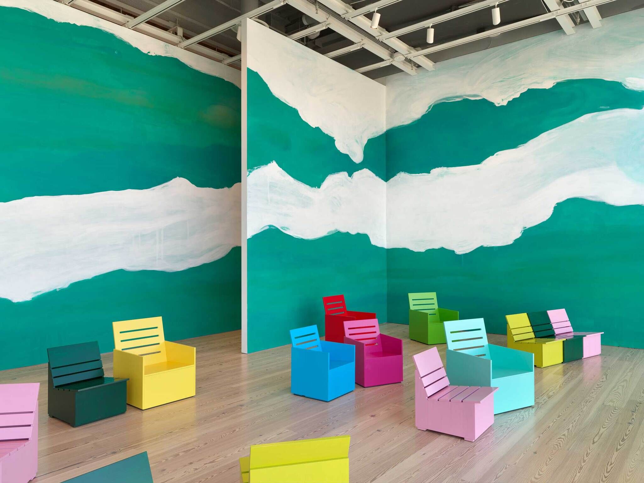 Room with green and white painted walls, featuring several colorful box-shaped chairs arranged on a wooden floor.