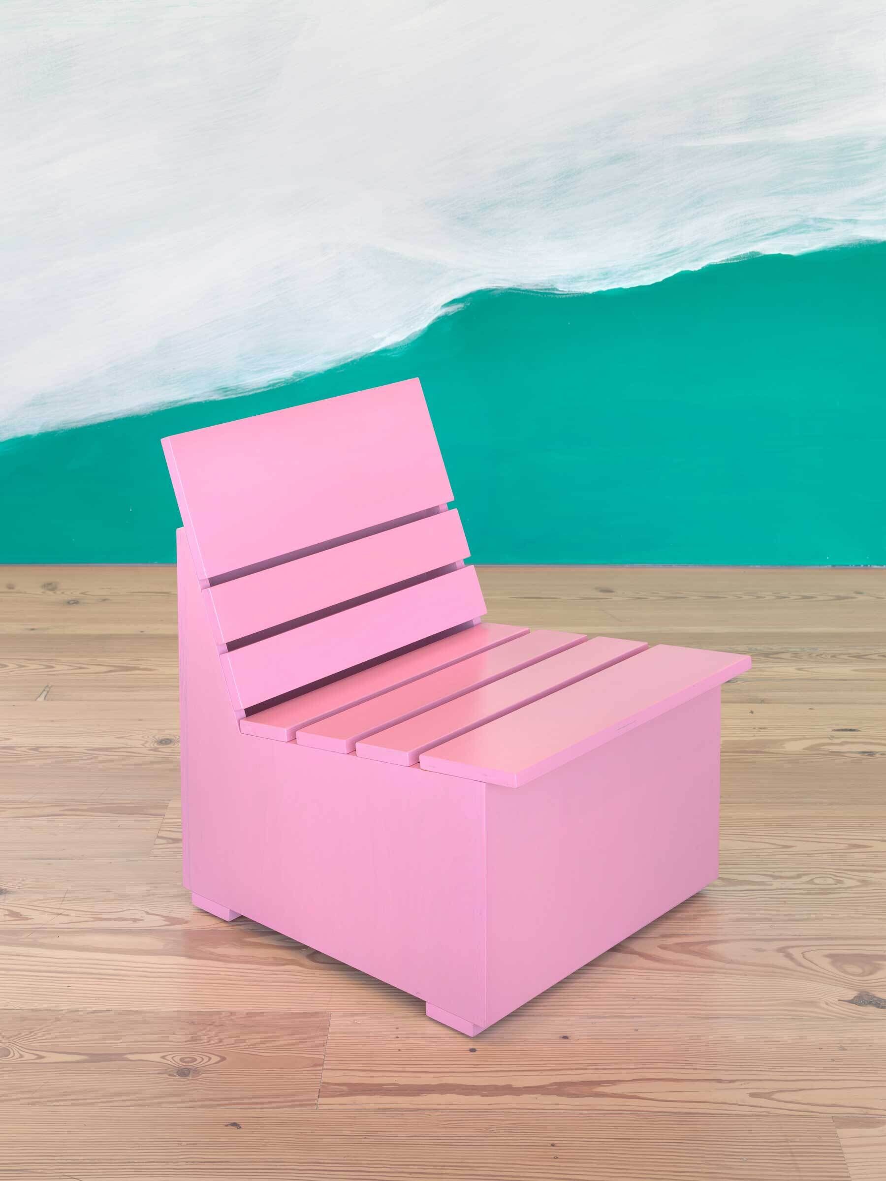 A simple pink wooden chair with slats sits on a light wood floor in front of a painted wall.