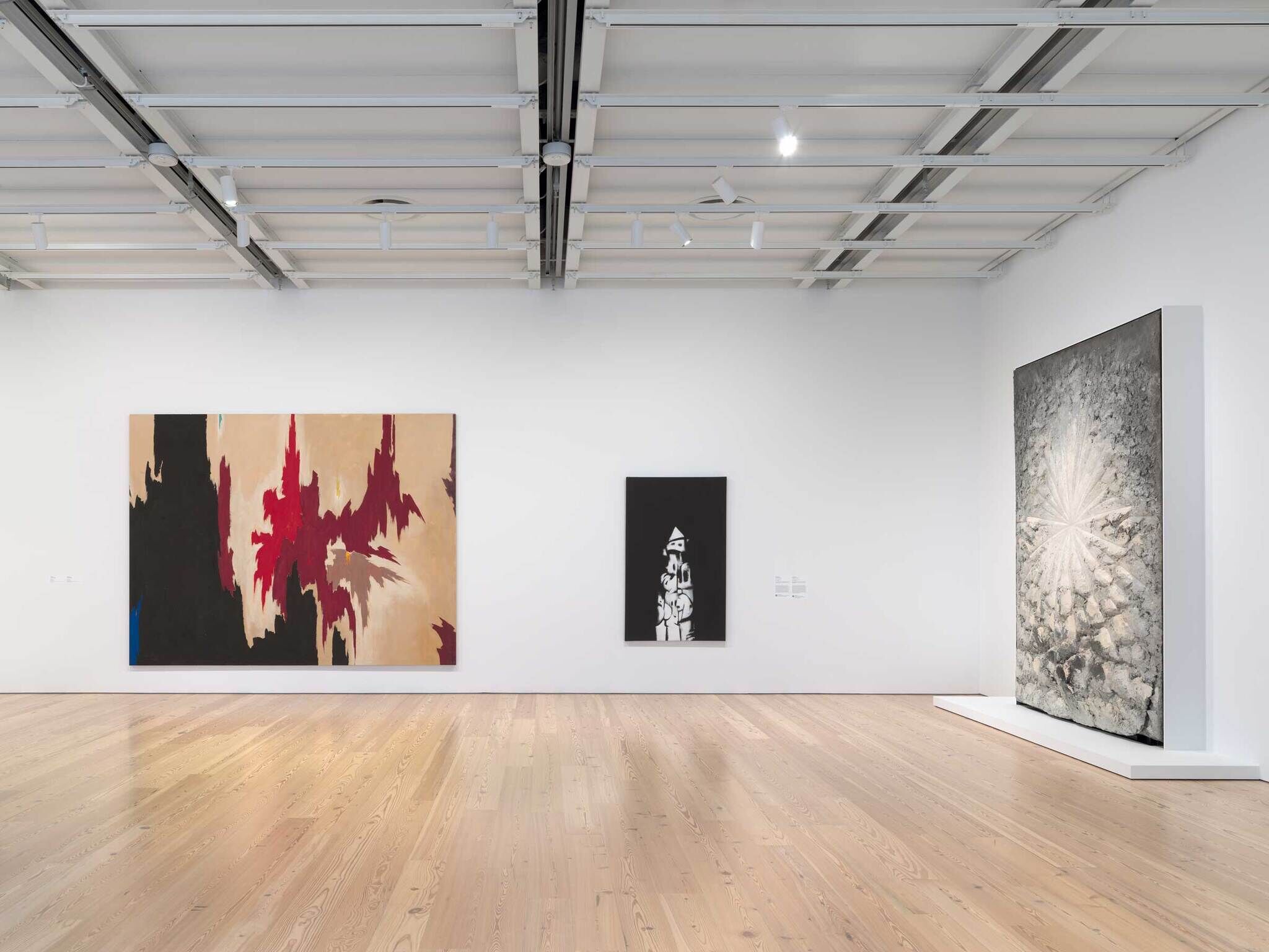 Three large abstract paintings hang on a white gallery wall, each with different colors and styles.