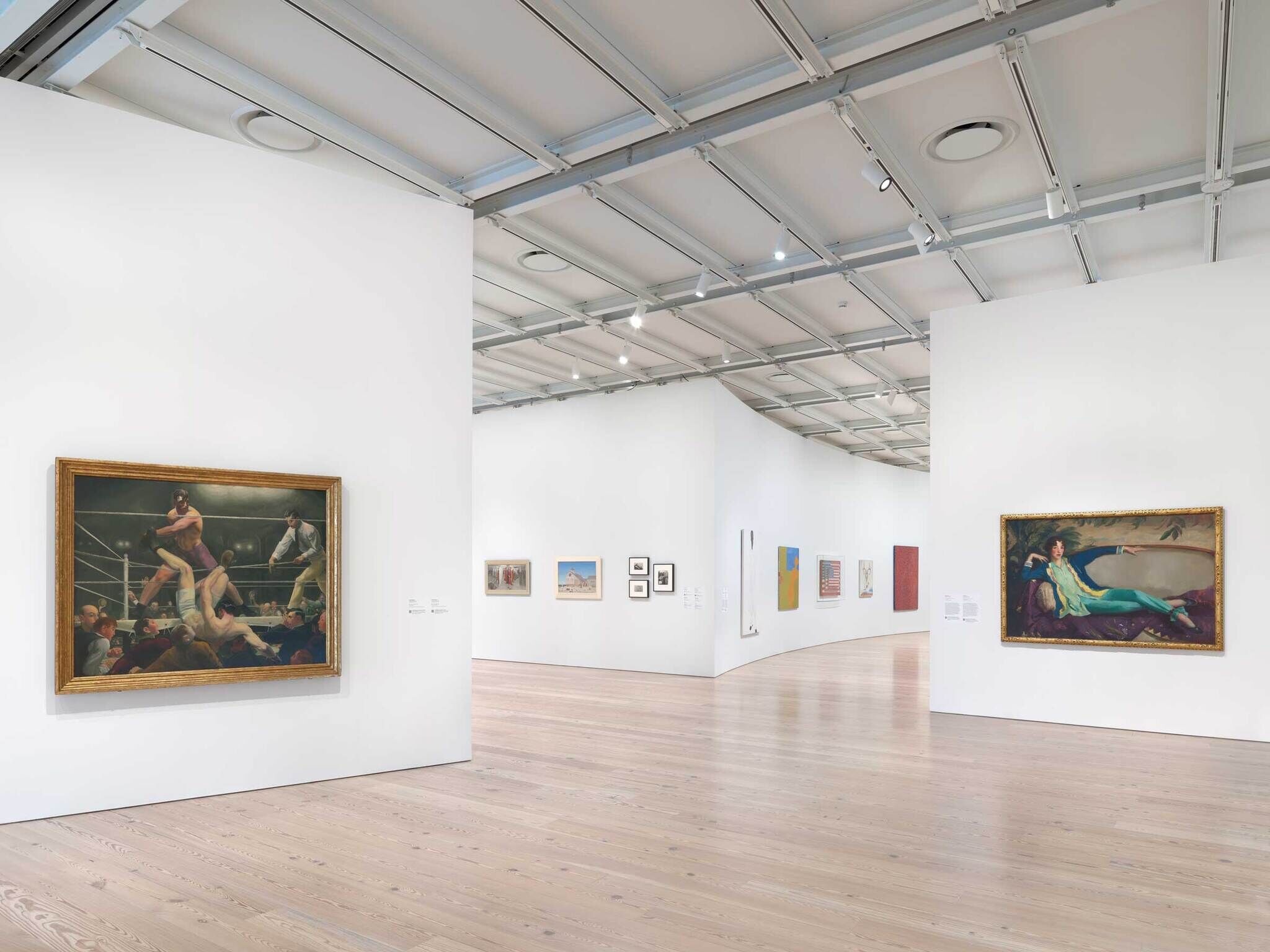 Spacious art gallery with large paintings on white walls, including a boxing scene and a reclining woman.