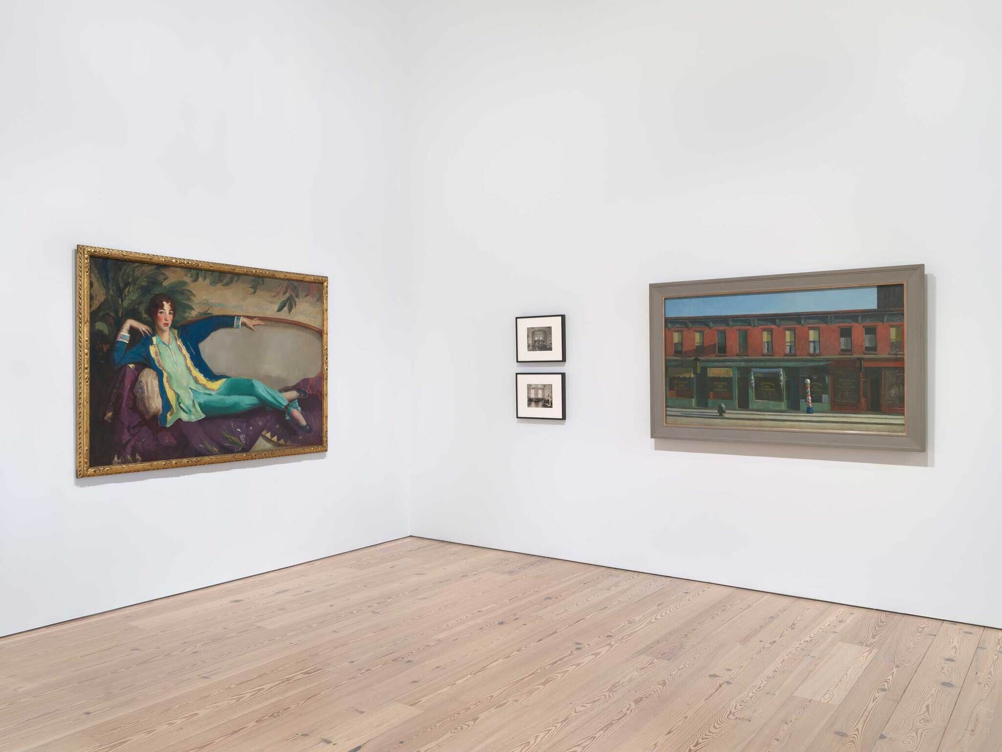 Art gallery room with a large painting of a woman on a couch, two small photos, and a cityscape painting.