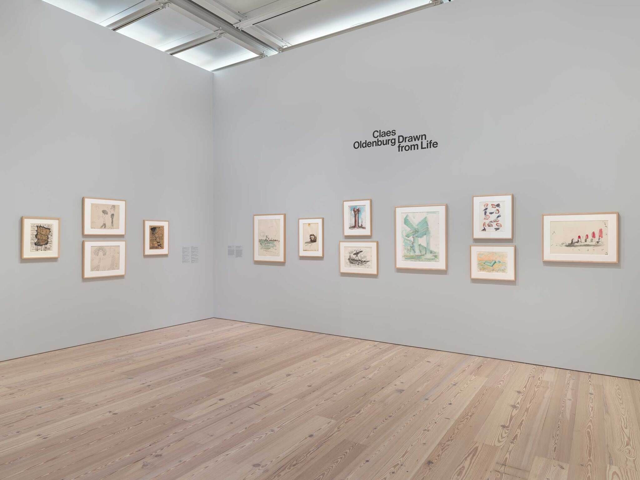 An art gallery with the words in black on the wall "Claes Oldenburg: Drawn From Life" with colorful framed sketches all around. 