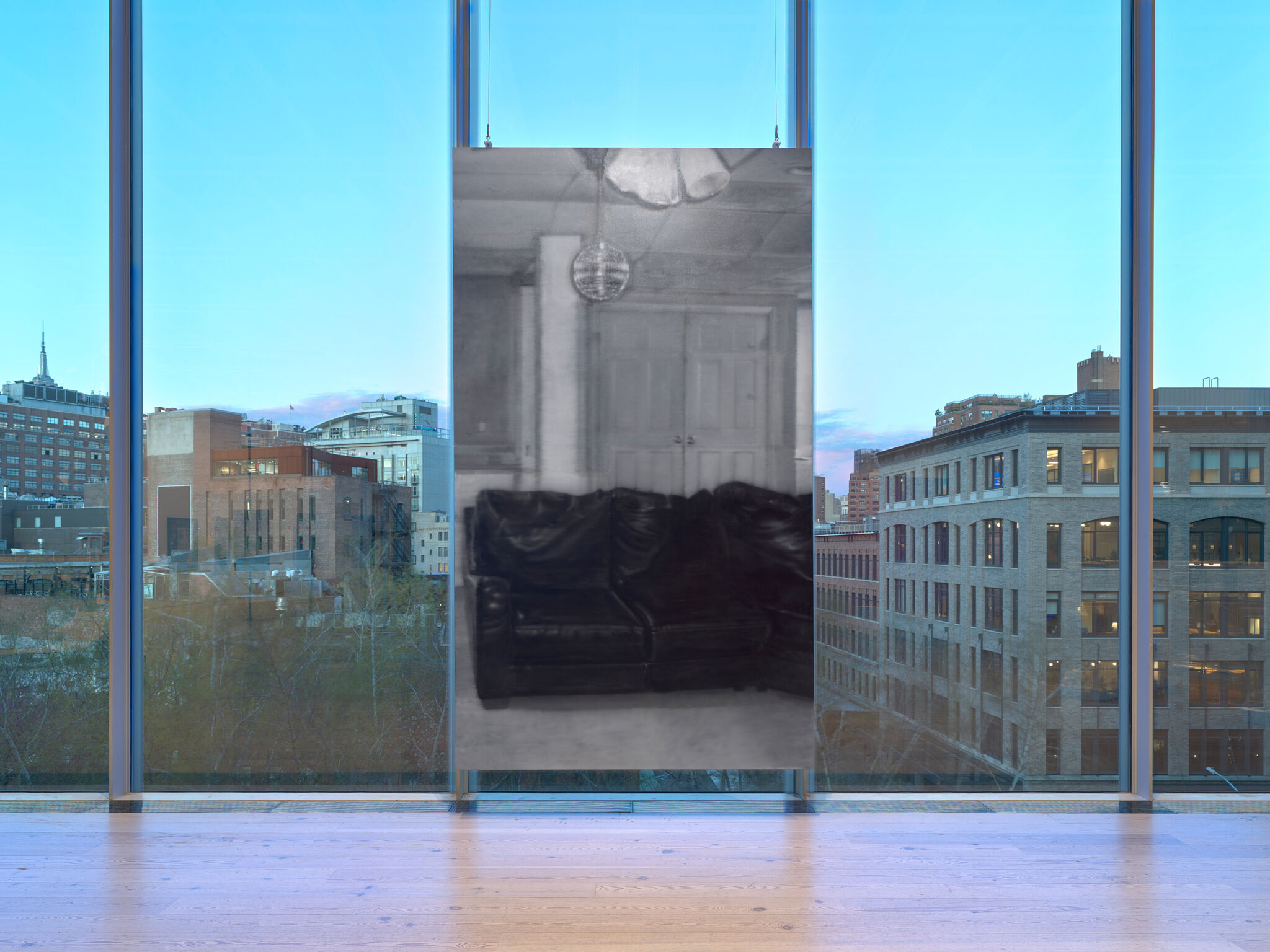 A panting hung in the middle of a window with a view of the city.