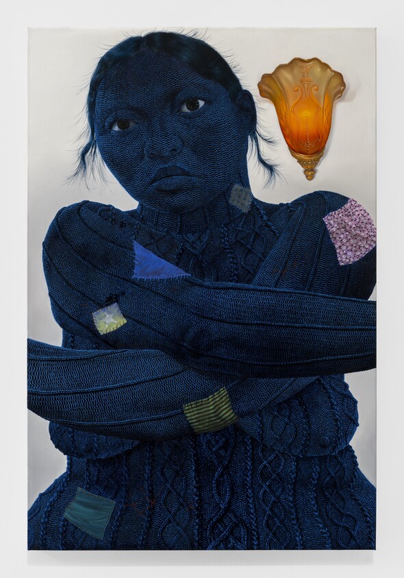 Person with dark blue textured skin and crossed arms, wearing a patched sweater, with an orange wall sconce above.