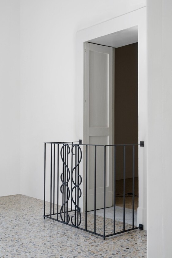 A black metal safety gate with a decorative pattern blocks an open doorway in a white room.